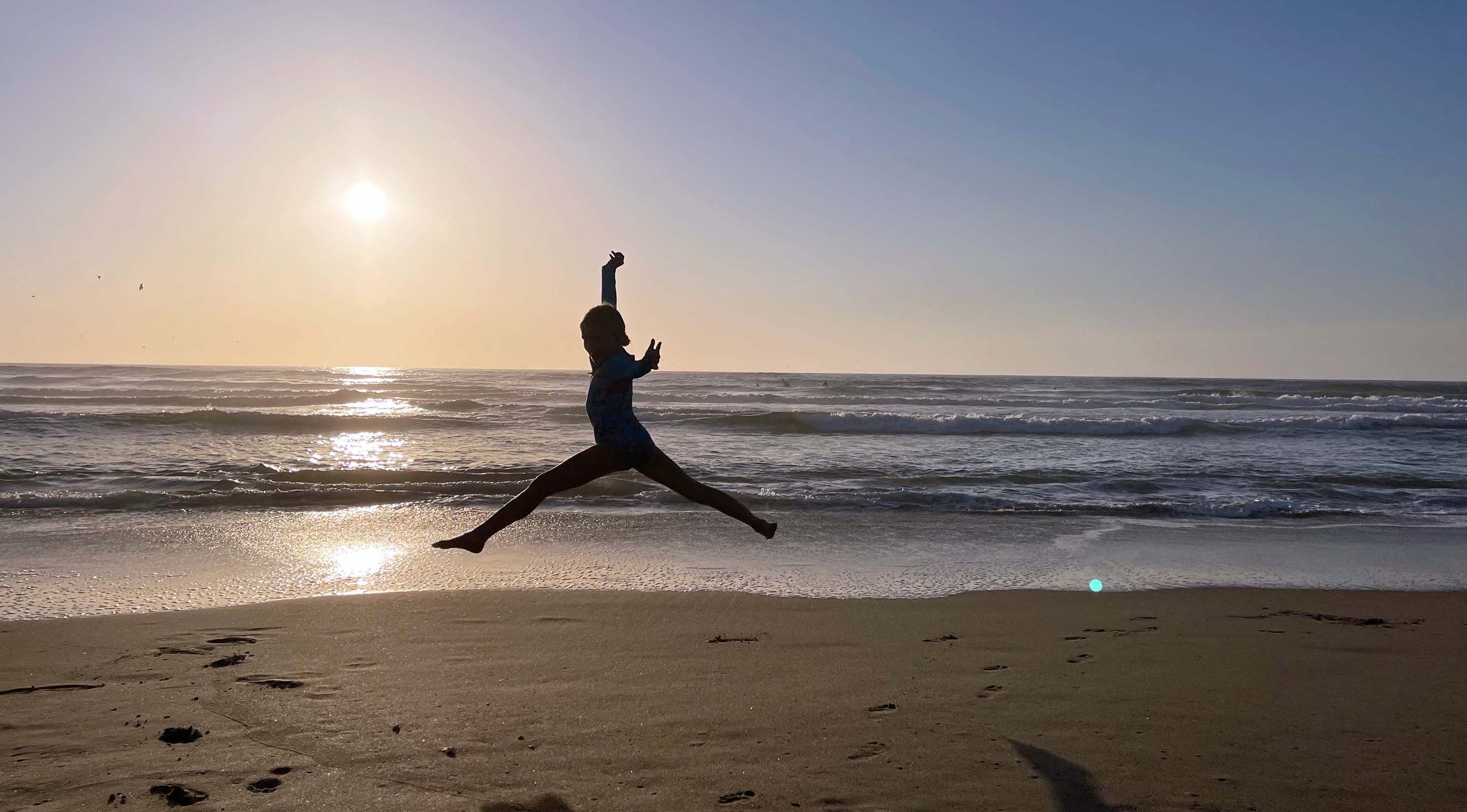 View of a child jumping on the beach at sunset