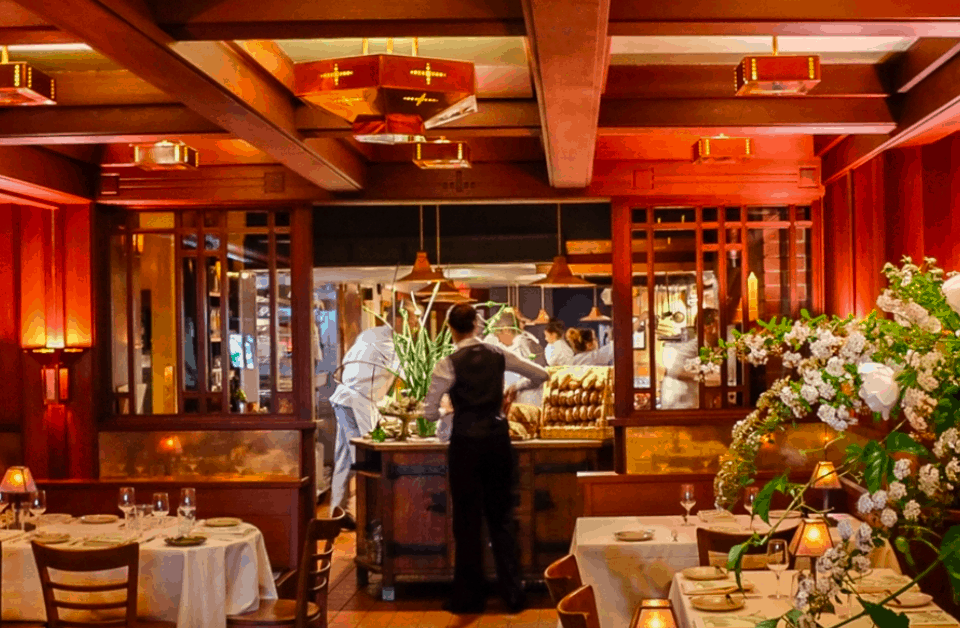 A waiter stands towards the back of a restaurant, among tables with white table cloths